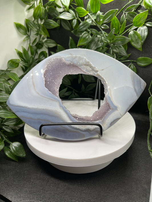 A large eye shaped crystal on a stand. The crystal is a blue agate with druzy quartz on the opening to the portal. 